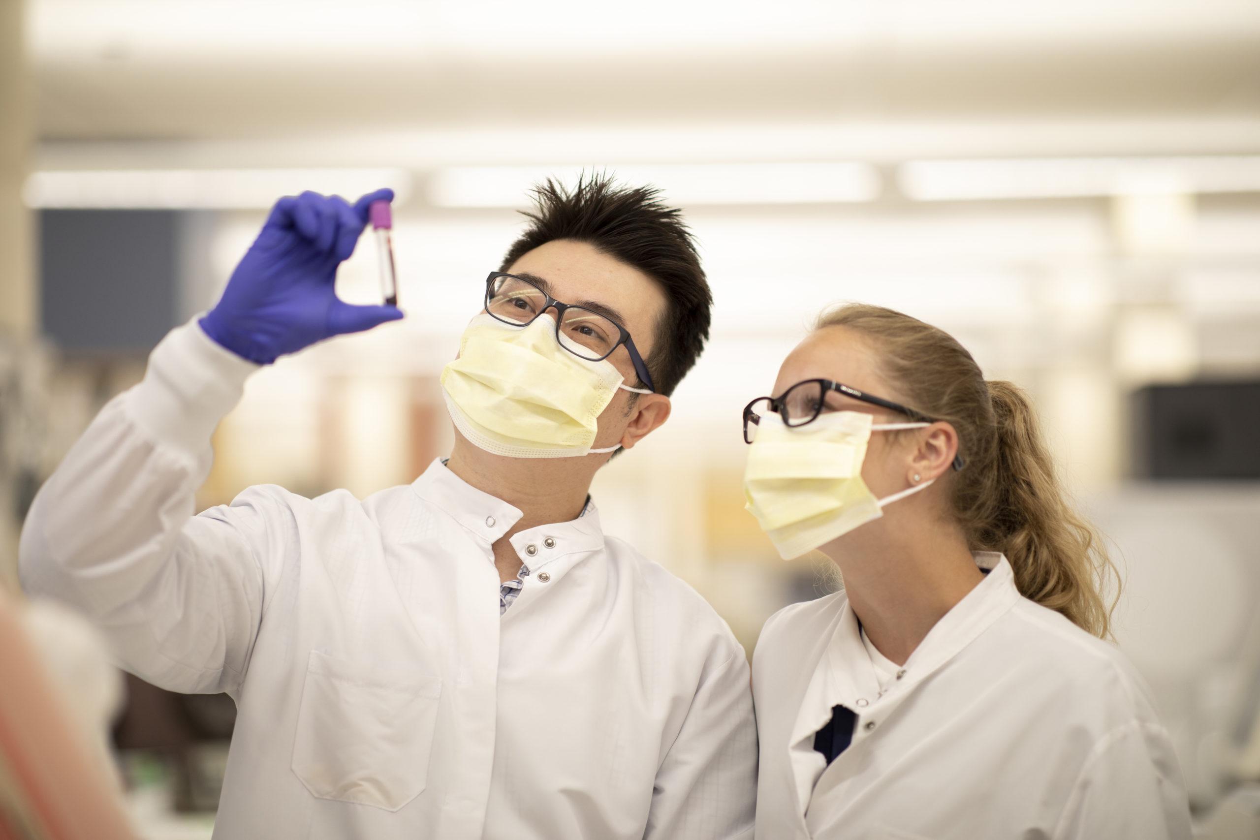两名身穿实验室服和口罩的人检查试管样品.